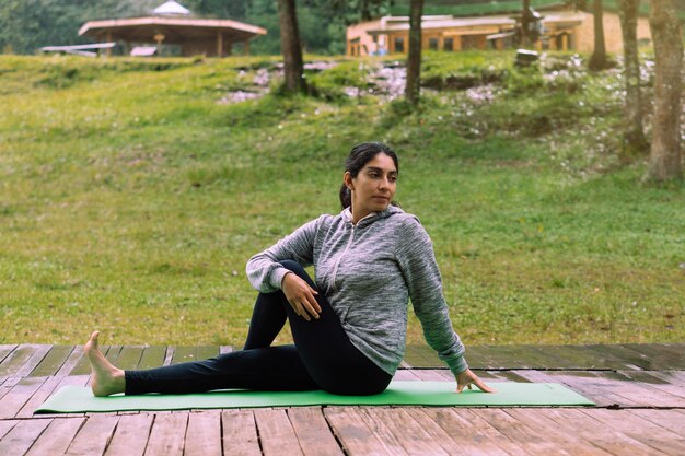 Woman alone in a forest practicing yoga in a forest, wearing sportswear and a mat.