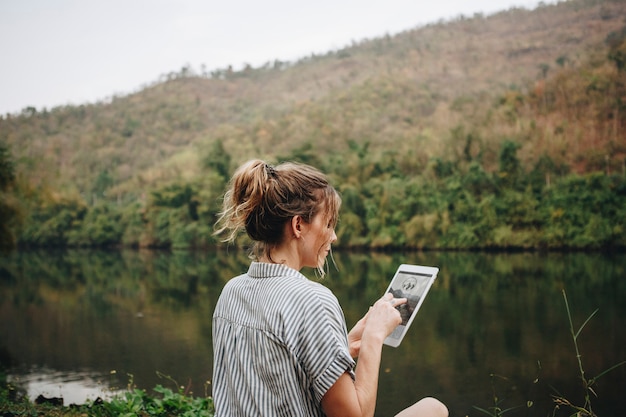 女性は、デジタルタブレットインターネット接続と旅行の概念を使用して自然の中で一人