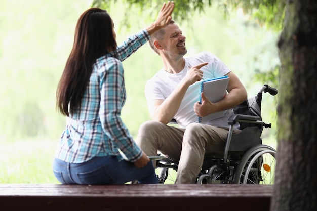 写真 車椅子の女性と男性が公園で勉強している人にこんにちは