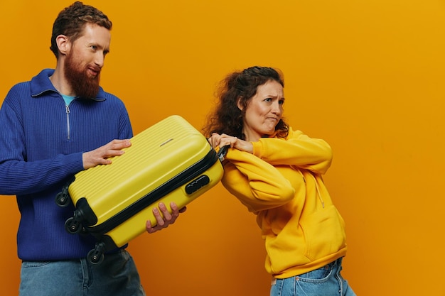 写真 黄色と赤のスーツケースを手に笑顔の女性と男性が楽しそうに微笑み、曲がった黄色の背景が旅行に行く家族休暇旅行新婚夫婦