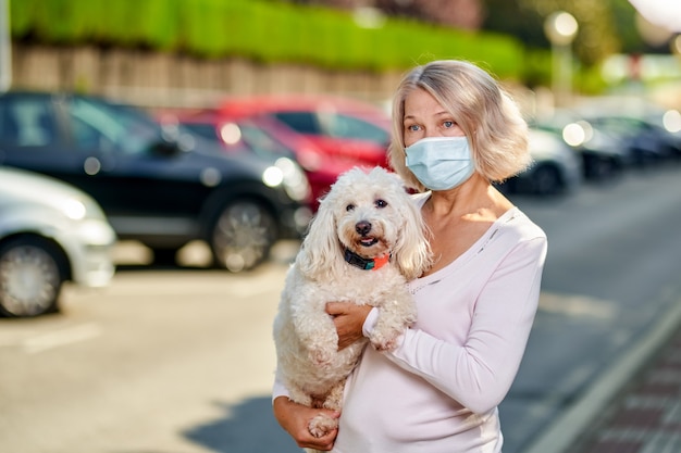 Woman an antivirus mask with a dog on a city street .