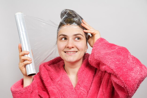 A woman applies a mask to her hair and wraps a film around her head