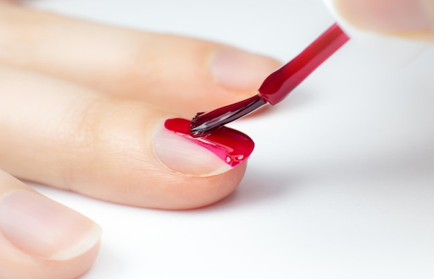 Foto donna applica lucchetto rosso per unghie ragazza che fa una manicure procedure di salone a casa belle mani e unghie foto macro in primo piano