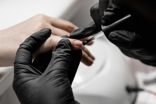 Woman apply varnish on nails manicurist in black rubber gloves