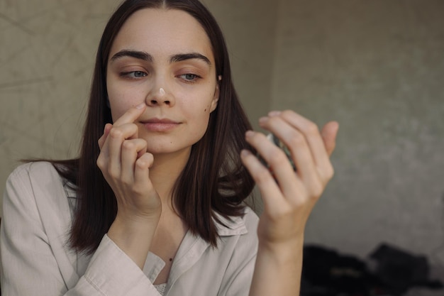 woman applying face cream and looking in mirror while doing daily beauty skin care routine