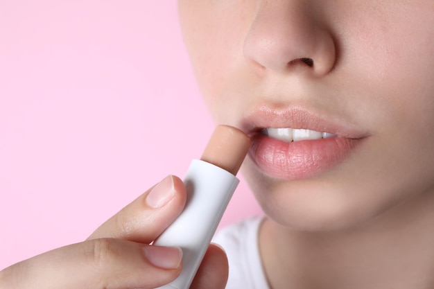 Woman applying hygienic lipstick on lips against pink background closeup