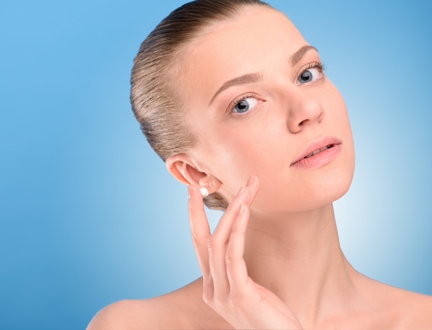 Woman applying lifting cream on face over blue background.