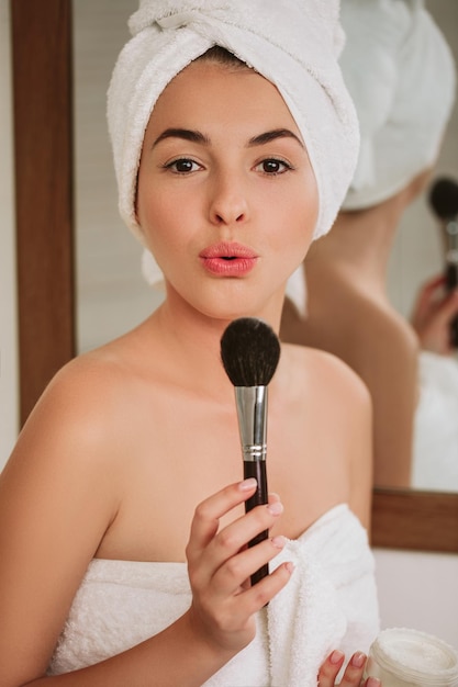 Woman applying makeup on face at home