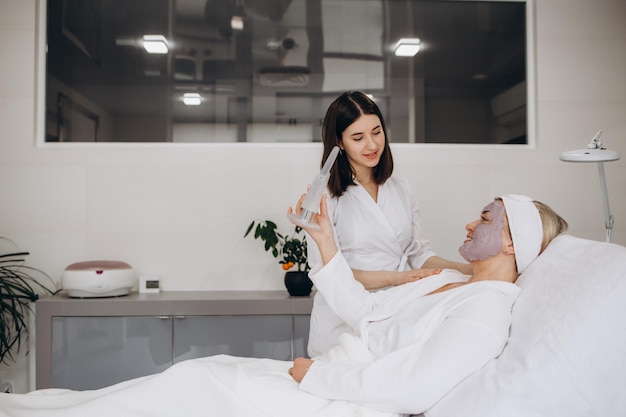 Woman applying mask on her face and looking in the mirror woman applying natural facial mask