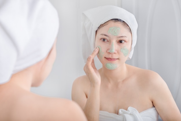 Woman applying mask on her face and looking in the mirror