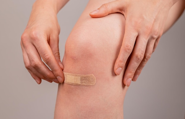 Woman applying medical plaster on knee first aid concept cuts\
abrasions and lightly bleeding wounds healing infection\
prevention