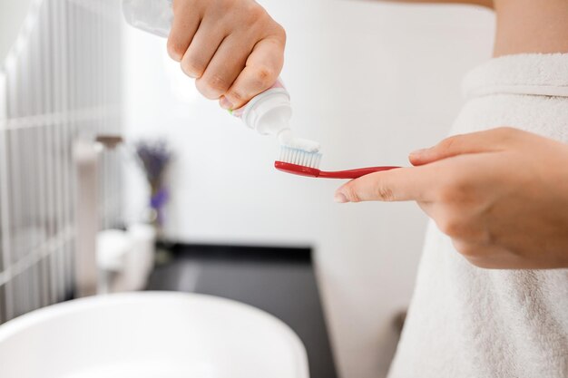 Женщина наносит зубную пасту на щетку в ванной комнате