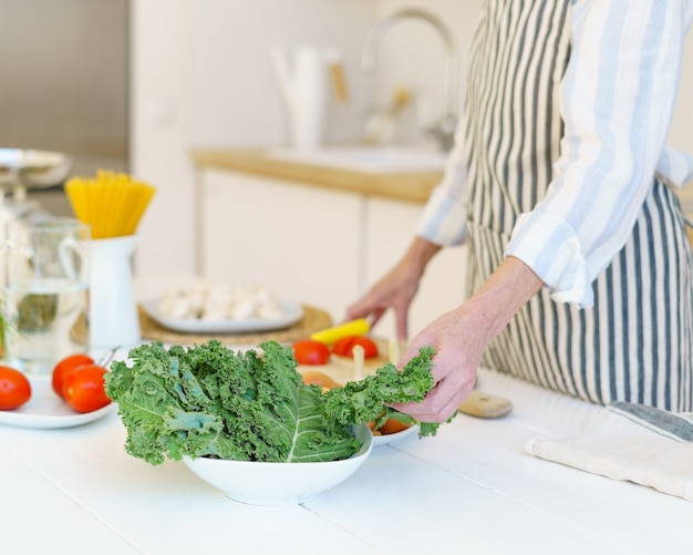 自宅のキッチンで料理をしながら野菜サラダを準備するエプロンの女性