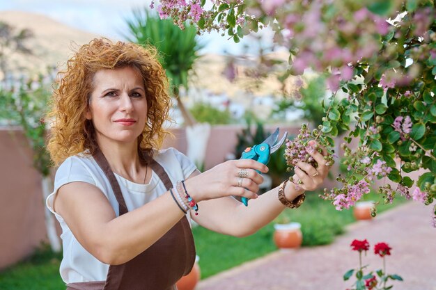 Женщина в фартуке с цветущим кустом секатора в саду