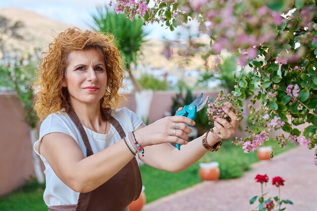 Woman in an apron with pruner flowering bush in garden