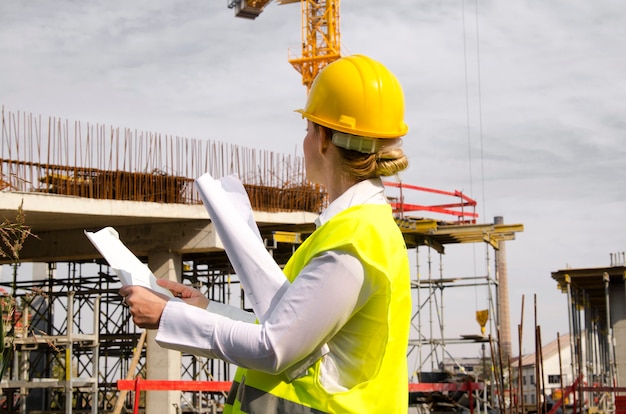 Woman architect at construction site with plans in hands looking at new building