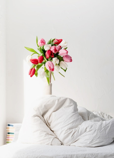 Photo woman arm outstreched from the blanket holding a bouquet of tulip flowers. woman in bed holding tulip flowers