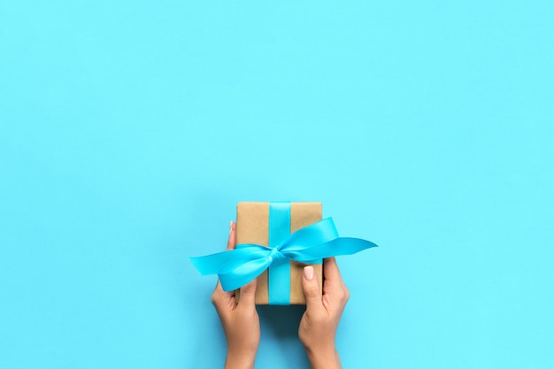 Woman arms holding gift box with blue ribbon on color , top view