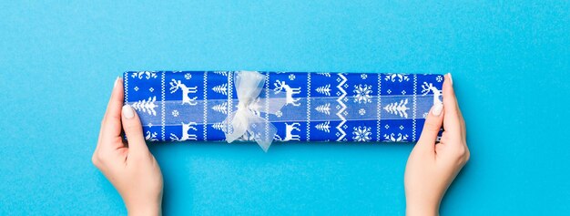 Photo woman arms holding gift box with colored ribbon on blue table background top view and copy space