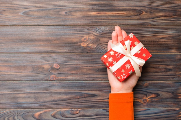 Woman arms holding gift box with colored ribbon on dark wooden table background