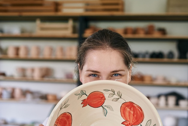 Woman artisan ceramist peeking out from behind clay products close-up