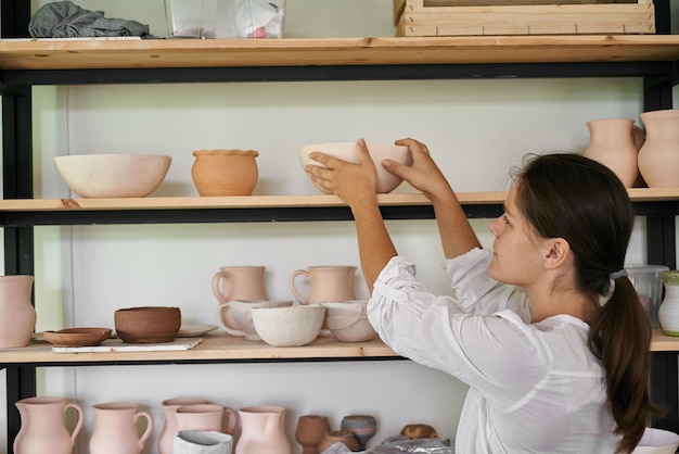 Woman artisan ceramist puts on a rack a bowl of handmade clay