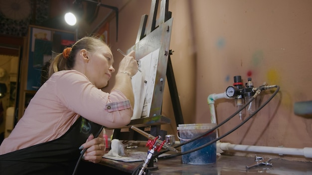 Photo woman artist learns to paint with airbrush with acrylic dye paper and easel indoors