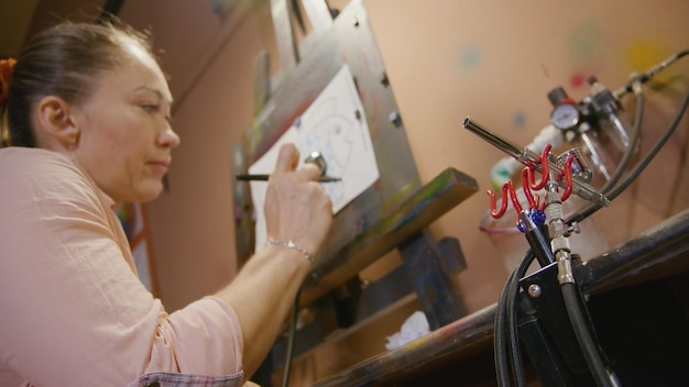 Photo woman artist learns to paint with airbrush with acrylic dye paper and easel indoors