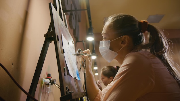여성 예술가는 아크릴 염료 종이와 이젤로 에어브러시로 그림을 그리는 법을 배웁니다.