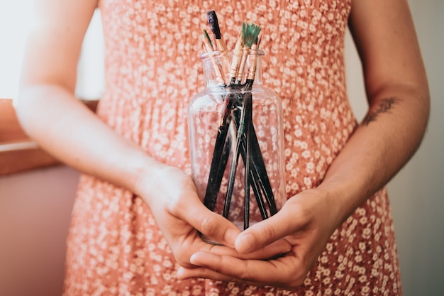 Woman artist painter holding a bunch of paint brush. Painter artist and paintbrush in studio, Crystal bottle, indie style, hipster, creative concept