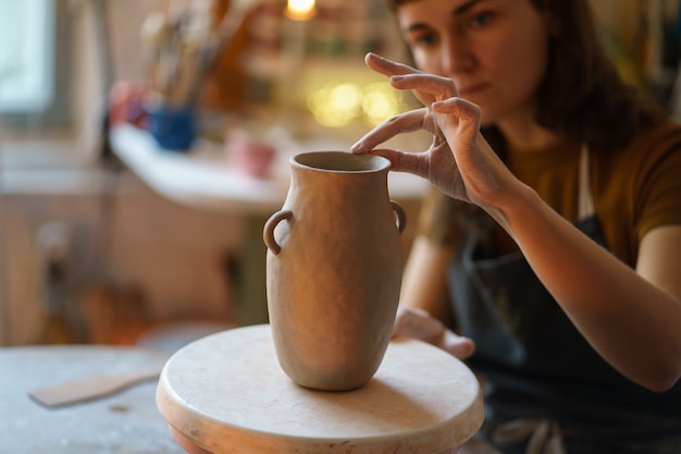 陶器工房の水差しの細部を形作る女性アーティスト若い女性が手作りのプロセスでリラックス