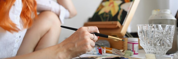 한 여성 예술가가 셔츠를 입은 여성의 손에 붓을 들고 그림 앞에 앉아 있다