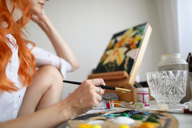 Photo a woman artist sits in front of a painting with a paintbrush in her hands woman in shirt at