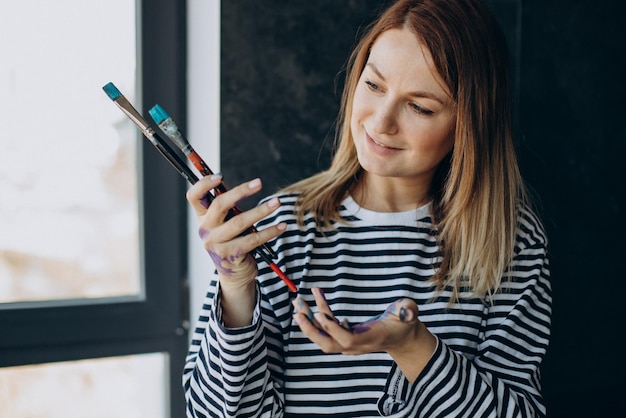 Woman artist with with painted hands holding brushes