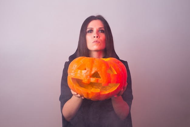 Woman as witch is standing with the pumpkin in the studio. Halloween and carnival concept