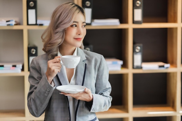 L'asiatico della donna si rilassa il ritratto bevente felice della tazza di caffè del mattino della tazza sorridente della ragazza al caffè del mattino