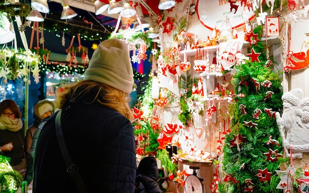 Фото Женщина у керамических елочных украшений на рождественской ярмарке на площади жандарменмаркт в зимнем берлине, германия. адвентская ярмарка украшения керамики и прилавки с поделками на базаре.
