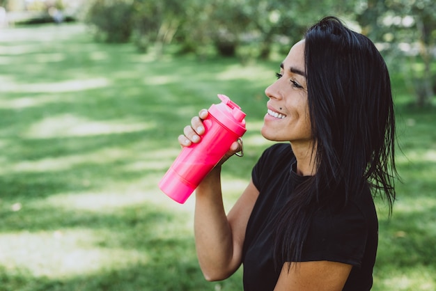 Woman athlete with a big fitness ball drinks protein from a shaker after training