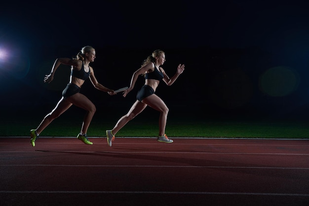 woman athletic runners passing baton in relay race