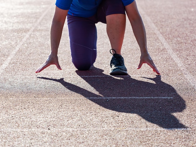 Donna sulla pista di atletica leggera esercizi nella posizione della linea di partenza e donna sportiva