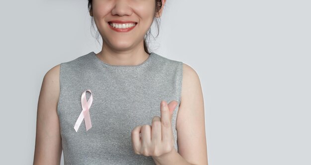 여성은 가슴에 분홍색 리본 활을 달고 가슴 앞에서 미니 하트 제스처를 만들어 유방암 환자를 격려합니다. 10월 달의 유방암 캠페인