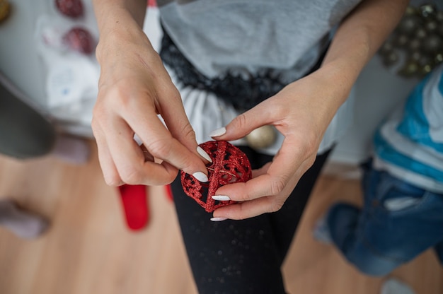 woman attaching golden string to a shiny red holiday bauble