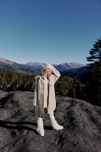 Woman in autumn clothes stands on a rock blue sky\
lifestyle