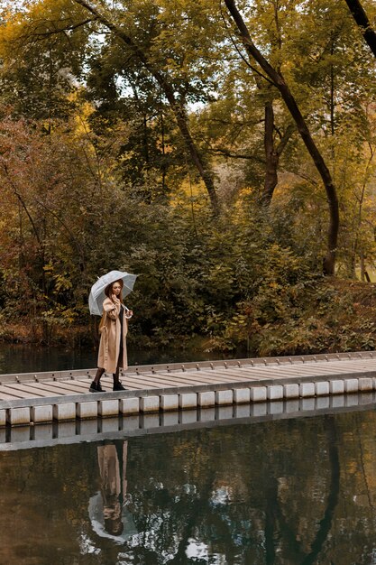 秋の都市公園を散歩する傘をさした秋の服を着た女性