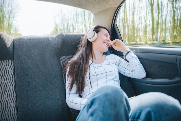 ヘッドセットで音楽を一覧表示する車の車の旅行の概念の後部座席の女性