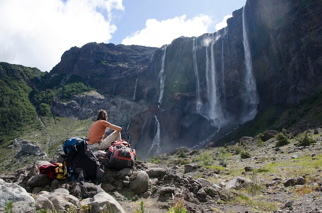 woman backpacker seated looking at the waterfalls of the volcano cerro tronador