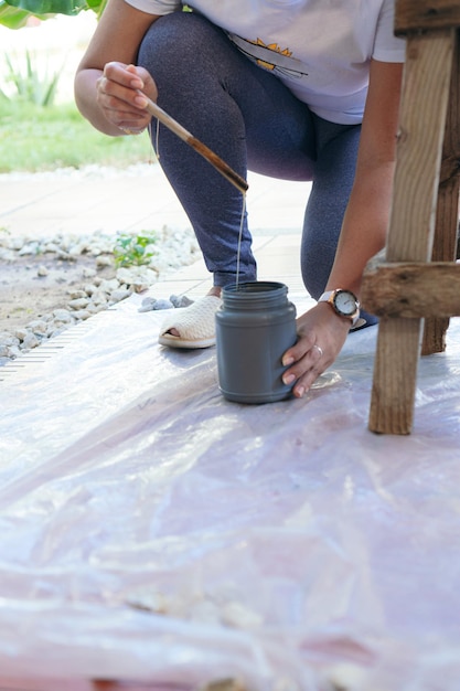 Woman in the backyard prepares a chair for restoration while holding a protective tape in her hand