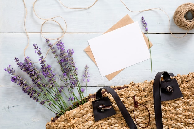 Фото Женская сумка с цветами лаванды, чистым листом бумаги и конвертом на синем деревянном столе