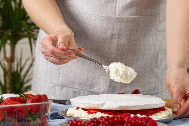 Woman baker adds whipped cream to the strawberry cake homemade strawberries cake made from meringue cake and cream with strawberries