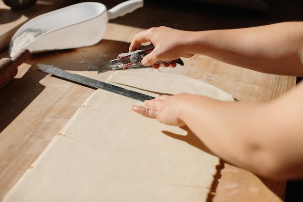 女性のパン屋はクロワッサンのために生地を三角形にカットしますパン屋でクロワッサンを作る